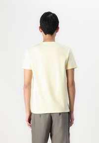 Lichtgele t-shirt met korte mouwen van zacht katoen, met een ronde hals en een relaxte pasvorm, gecombineerd met grijze linnen broeken.
