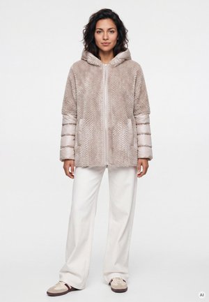Woman wearing beige textured hooded jacket with padded sleeves, white wide-leg pants, and beige sneakers, standing against plain white background.