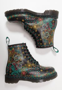 Botas negras con cordones que presentan un colorido patrón de flores y calaveras. Cuentan con una suela texturizada y detalles en azul verdoso a lo largo de la costura y el borde superior.