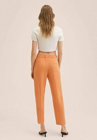 Hvid cropped sweater med korte ærmer, parret med højtaljede orange bukser, der har en baglomme og en glat overflade.