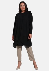 Black long-sleeve tunic with pleated front, sheer hem. Paired with beige tapered pants and light-colored high heels. Simple design.