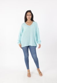 Jasnoniebieski, oversize sweter z dzianiny z dekoltem w serek, długimi rękawami i teksturowanym materiałem, noszony z dopasowanymi dżinsami i przezroczystymi sandałami na obcasie.