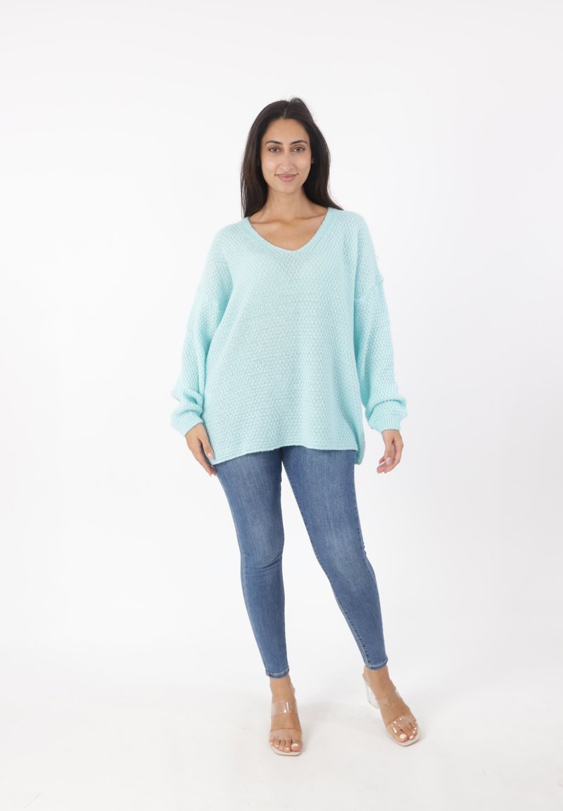 Jasnoniebieski, oversize sweter z dzianiny z dekoltem w serek, długimi rękawami i teksturowanym materiałem, noszony z dopasowanymi dżinsami i przezroczystymi sandałami na obcasie.