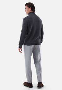 Grauer Wollpullover mit hohem Kragen, kombiniert mit hellgrauen Hosen und braunen Schuhen. Schlichtes Design mit gerippten Bündchen und Saum.