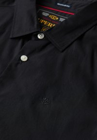 Polo nera in cotone con colletto a punta, due bottoni bianchi e logo ricamato discreto sul lato sinistro del petto.