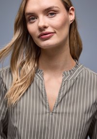 Chemise gris clair à col avec rayures blanches verticales, dotée d'un décolleté en V et d'une texture lisse légèrement brillante. Design simple et moderne.