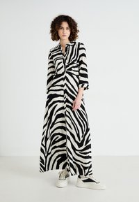 Robe longue à rayures noires et blanches, avec un col, un devant à boutons et des manches trois-quarts, associée à des baskets blanches.