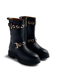 Botines de cuero negro con acentos de hardware circular dorado, cierre de cremallera y detalle de correa con hebilla. Suela de goma negra gruesa.