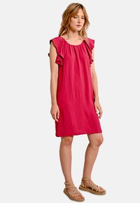 Abito fucsia con maniche arricciate, taglio morbido e scollatura rotonda. Realizzato in materiale leggero, arriva appena sopra le ginocchia.