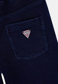 Leggings in denim blu scuro con tasca posteriore decorata da una patch triangolare nei colori rosso, bianco e blu. Tessuto liscio con leggera elasticità.