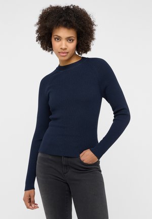 Maglione a costine in blu navy con maniche lunghe e scollo rotondo, caratterizzato da un design aderente e una texture sottile, abbinato a jeans scuri.