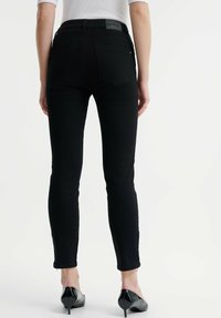 Crne skinny traperice s srednjim strukom, pet džepova i diskretnim detaljima šivanja, u paru s cipelama s oštrim vrhom.