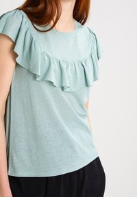 Ljusblå kortärmad topp med rynkad halsringning och texturerad tyg. Designad med en avslappnad passform och slät yta.