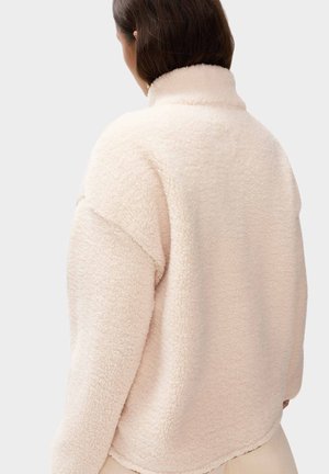 Cremefarvet fleecejakke med høj krave, løs pasform og tekstureret stof, der har dropped shoulders og en let buet kant.