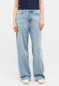 Jasnoniebieskie dżinsy w szerokim kroju, wykonane z denimu, z wysokim stanem, czterema kieszeniami i lekko wybledzonym wykończeniem. Stylizowane z granatową bluzką.