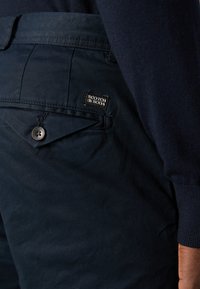 Marineblauwe shorts van katoen met een knoopsluiting en een label met de tekst "SCOTCH & SODA" op de achterzak. Smalle textuur en een getailleerde pasvorm.