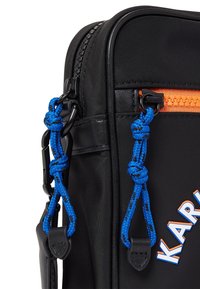 Borsa nera in nylon con zip arancione, dettagli in corda blu e branding 'KARL'. Texture liscia con forma rettangolare e hardware robusto.