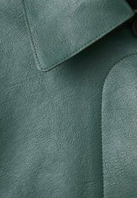 Tejido de cuero verde con una superficie texturizada, que presenta un cuello y detalles cosidos. Variación de color visible y brillo en el material.