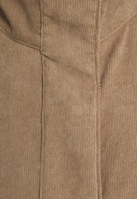 Nahaufnahme von braunem Cordstoffen, die vertikale Rippungen und Details einer mittigen Naht zeigen.