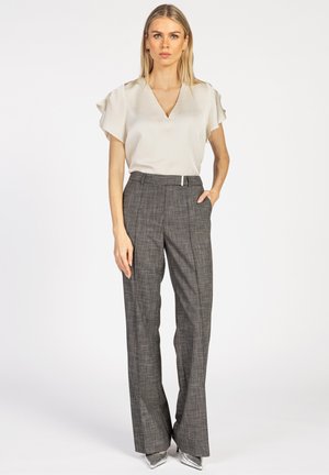 Hellbeige V-Ausschnitt-Bluse mit kurzen, schwingenden Ärmeln, kombiniert mit grauen karierten, hoch taillierten Hosen und silbernen spitzen Absatzschuhen.