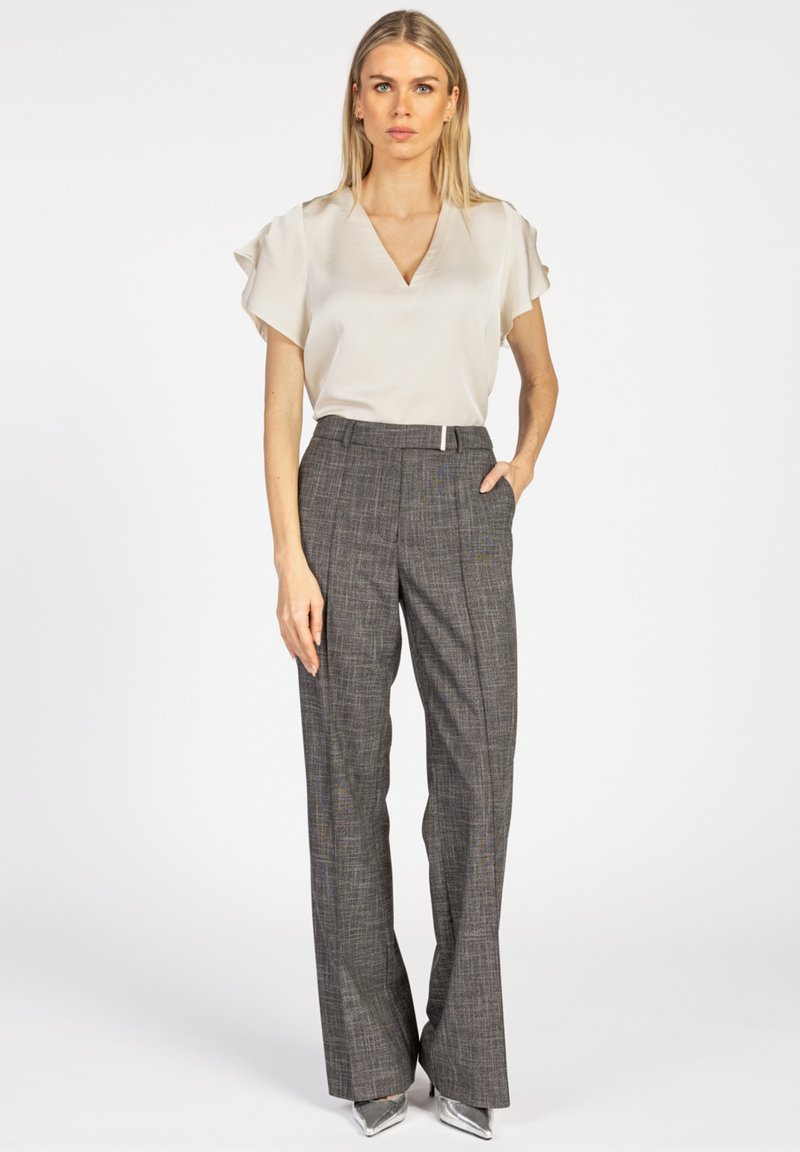 Lichtbeige V-hals blouse met korte fladdermouwen, gecombineerd met grijs geruite hoge taille broek en zilveren puntige hakken.