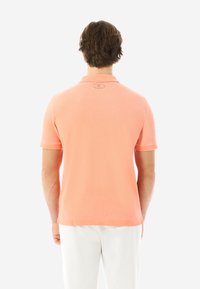 Kurzarm-Polohemd in Korallenfarbe, aus weichem Baumwollstoff. Verfügt über einen klassischen Kragen, gestickte Akzente und ein kleines Markenlabel.