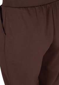 Braune, weiche Stoffhosen mit einem elastischen Bund und Seitentaschen, die eine glatte Textur und einen lockeren Schnitt bieten.