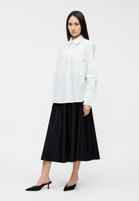 Λευκό πουκάμισο με μακριά μανίκια και κουμπιά, συνδυασμένο με μαύρη φούστα μήκους μέχρι το γόνατο. Μαύρα μύτα παπούτσια χωρίς τακούνι ολοκληρώνουν το σύνολο.