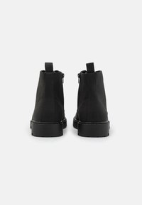 Botas negras de tobillo con una textura de ante suave, cierres de cremallera lateral, lengüetas de agarre en bucle y un diseño de punta cuadrada sobre una suela gruesa de goma.