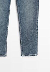 Dolna połowa niebieskich dżinsów na białym tle, z prostymi nogawkami i subtelnym efektem wyblaknięcia.