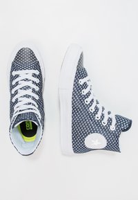 Pari sininen ja valkoinen korkea sneakers-jalkine, joissa on valkoiset nauhat ja tähden logo sivussa, esillä valkoisella taustalla.