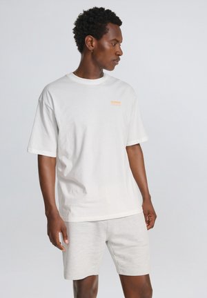 Vit bomull t-shirt med korta ärmar och rundad hals, med en liten orange logotyp. Tillsammans med ljusgrå shorts i mjukt material.