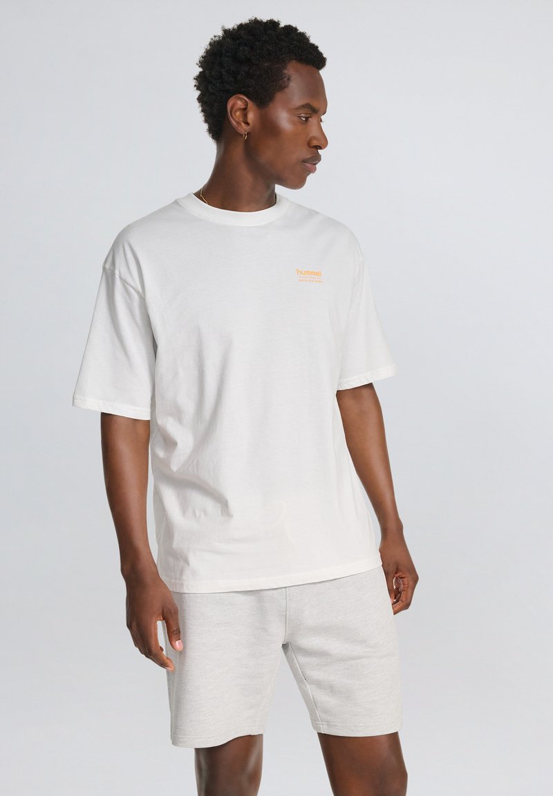 Hvid bomulds T-shirt med korte ærmer og rund hals, prydet med et lille orange logo. Sammen med lysegrå shorts lavet af blødt materiale.