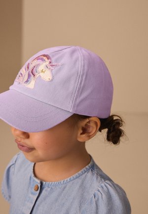 Niño/a con gorra lavanda con un parche de unicornio de lentejuelas, camisa azul claro y el pelo recogido en un pequeño moño.