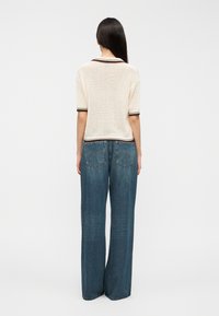 Haut en maille résille écru à manches courtes avec col et poignets marron, associé à un jean denim bleu à jambes larges avec poches arrière et surpiqûres.