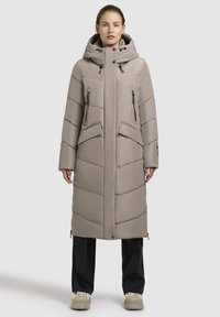 Lang, lys beige pufferjakke med hætte, horisontal og vertikal syning, to lynlåslommer og ribbede manchetter. Den har et elegant, minimalistisk design.