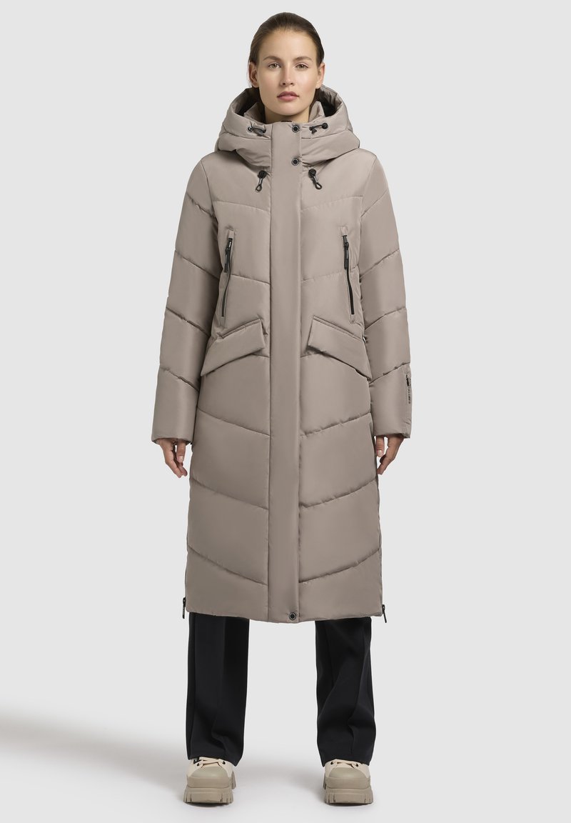 Lang, lys beige pufferjakke med hætte, horisontal og vertikal syning, to lynlåslommer og ribbede manchetter. Den har et elegant, minimalistisk design.