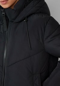 Schwarze Daunenjacke mit hohem Kragen und verstellbarem Kapuze. Sie verfügt über einen durchgehenden Reißverschluss, ein quilted Muster und einen zurückhaltenden Außenstoff.