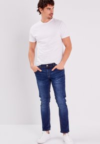 Valkoinen puuvillapaita yhdistettynä sinisiin skinny-farkkuihin, joissa on viisi taskua ja hieno haalistuminen. Täydentää asua valkoiset lenkkarit.