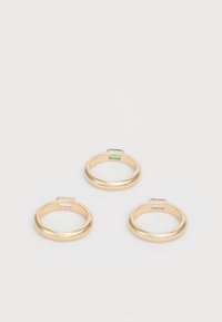 Tres anillos de oro con bandas suaves y redondeadas. Cada uno presenta un engaste rectangular para gema; los colores incluyen verde, transparente y rosa.