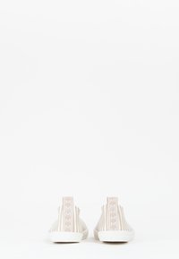 Scarpe slip-on a righe beige con suola in gomma bianca e un'etichetta sul tallone con il marchio. Texture liscia e design casual.