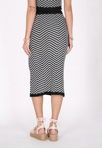 Rochie tricotată cu un model zigzag alb-negru, cu talie ajustată, care se termină sub genunchi, asortată cu sandale cu platformă de culoare deschisă.