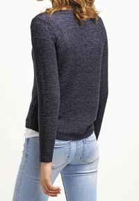 Pull en maille bleu foncé à manches longues, tissu texturé et encolure arrondie, associé à un jean ajusté bleu clair.