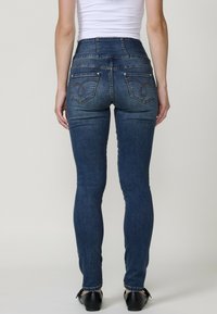 Jeans de denim de talle alto en azul oscuro con un corte ajustado, que cuentan con bolsillos traseros con costuras decorativas y acentos de hardware mínimos.
