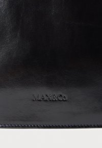 Dettaglio di un oggetto in pelle nera con bordo cucito e logo MAX&Co. impresso su superficie liscia.