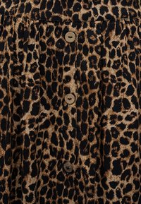 Tessuto a stampa leopardata con una fila verticale di tre bottoni rotondi color sabbia cuciti, che mostrano i dettagli della trama e del motivo.