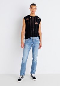 Top nero senza maniche con strappi orizzontali, jeans in denim blu chiaro e sneakers con motivo in bianco e nero. Design semplice e vestibilità rilassata.