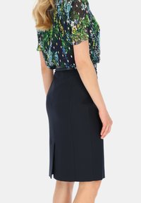 Granatowa spódnica ołówkowa z rozcięciem z tyłu, wykonana z gładkiego materiału, w zestawieniu z bluzką z krótkim rękawem w wielokolorowy wzór kwiatowy.