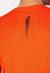 Orange sportströja med en texturerad tyg; har en svart vertikal randdesign på baksidan som framhäver andningsförmåga och stil.