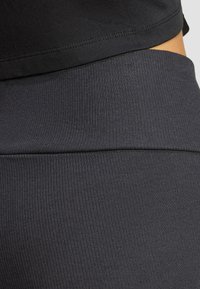 Svarta ribbade leggings med en slät textur och elastisk midja, delvis dolda av en svart topp vid midjan.